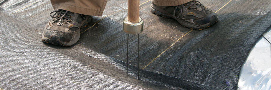 Person inserting staples to secure landscape fabric.