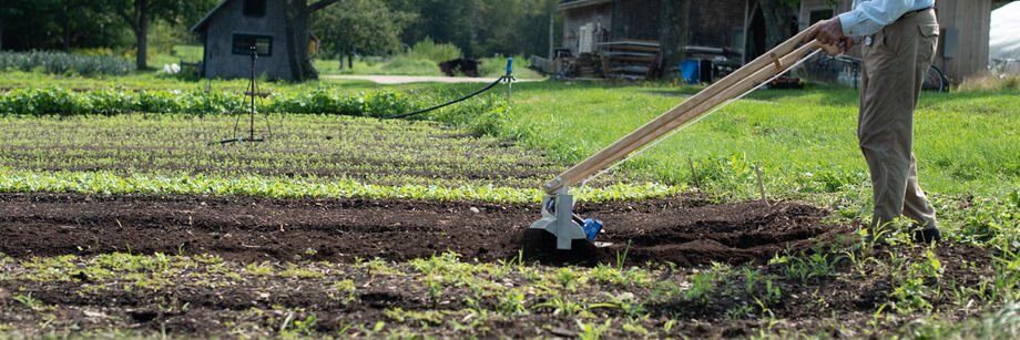 Person using a Tilther to till the top few inches of garden bed.