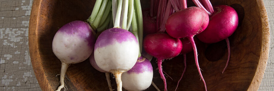 Red turnips and purple-top turnips, grown from Johnny's turnip seeds, and displayed in a wooden bowl.