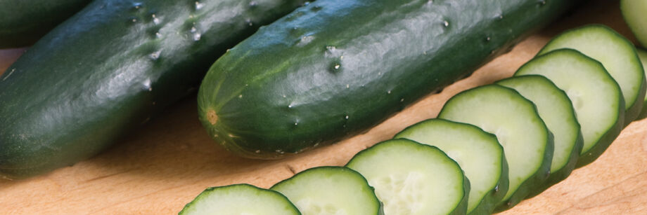 Sliced and whole cucumbers of one of Johnny's cucumber varieties, laid out on a wood cutting board.